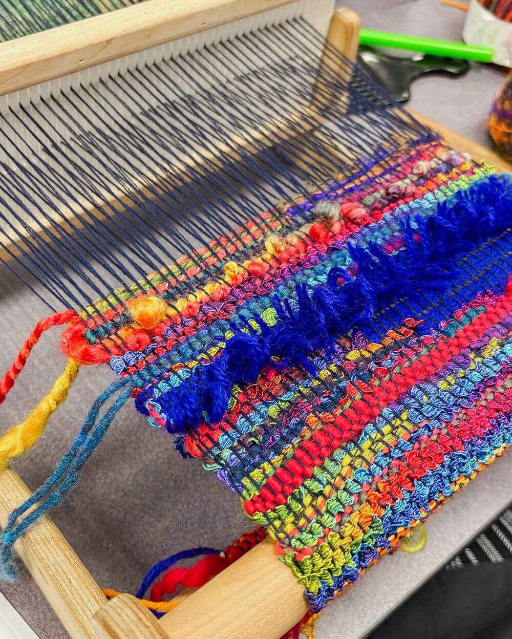 a closeup of a rigid heddle loom with colorful yarn woven on it