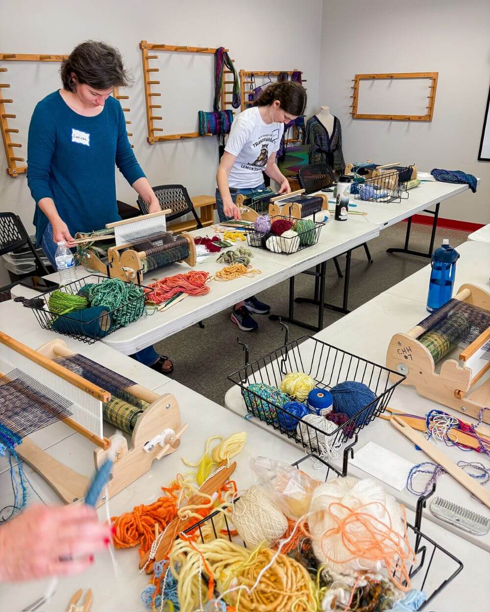 two women in a classroom are standing at a table learning how to weave