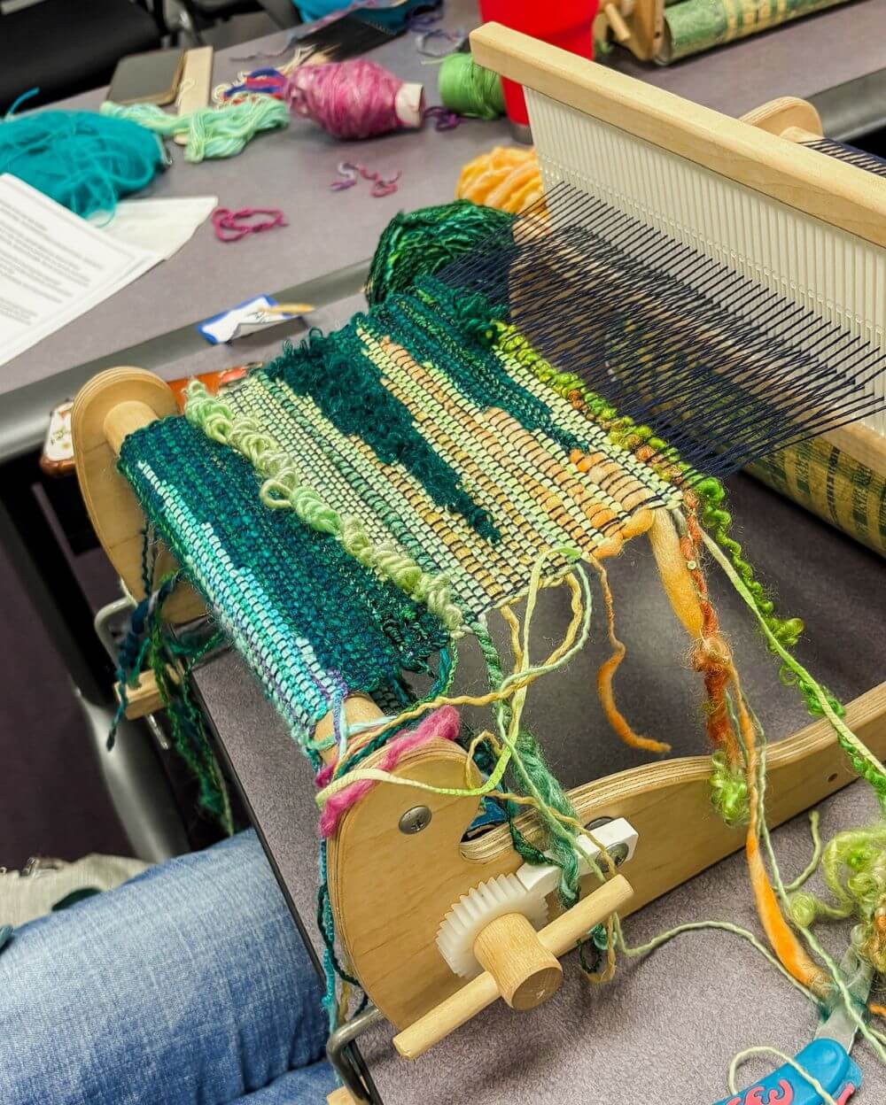 a closeup of a rigid heddle loom with green yarn woven on it