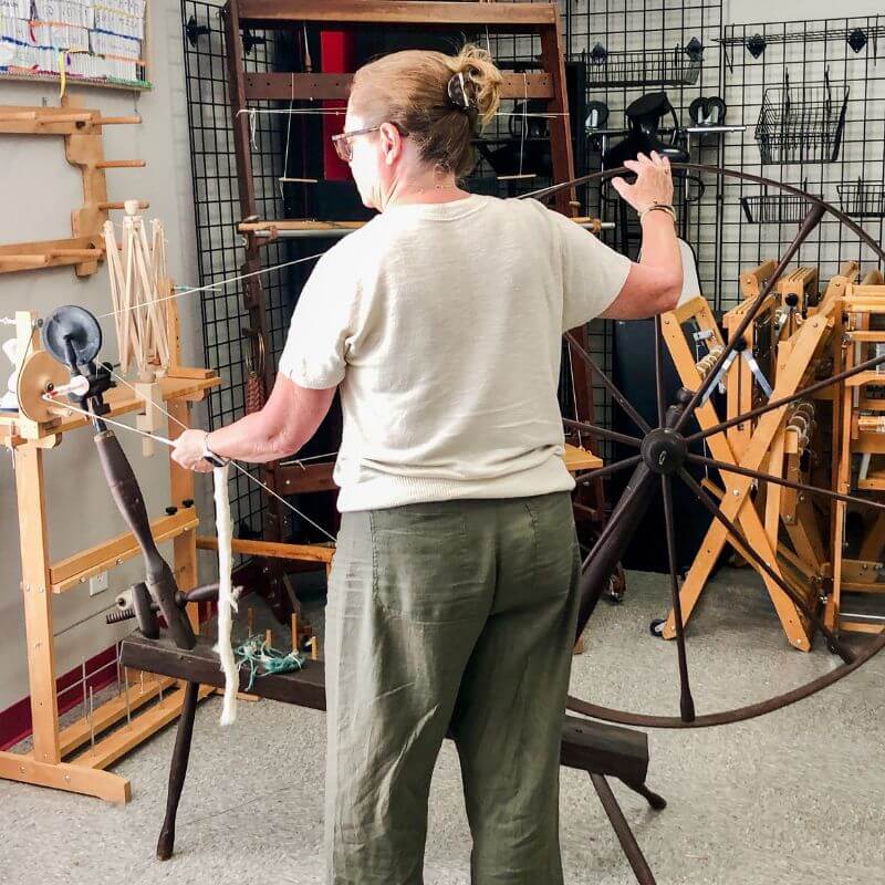 A woman practices spinning on a large antique spinning wheel.